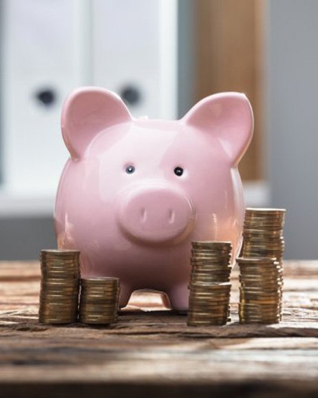 Close up of someone using a calculator with a piggy bank nearby 