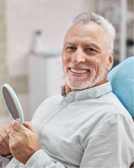 Senior man holding mirror and smiling in dental chair