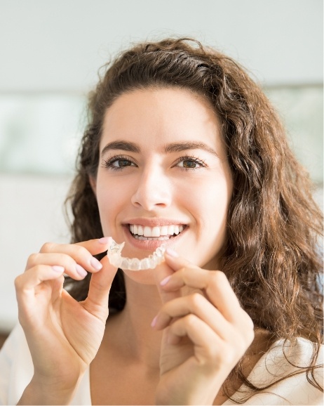 Smiling woman holding an Invisalign tray near her mouth