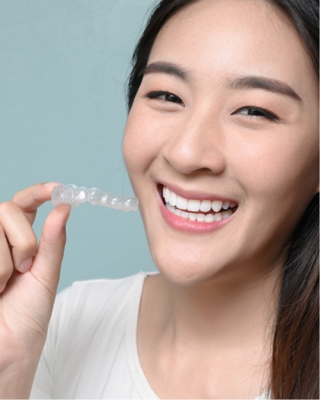 Smiling teenage girl holding an Invisalign aligner