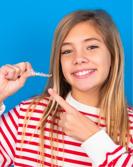 Young girl holding and pointing to Invisalign aligner