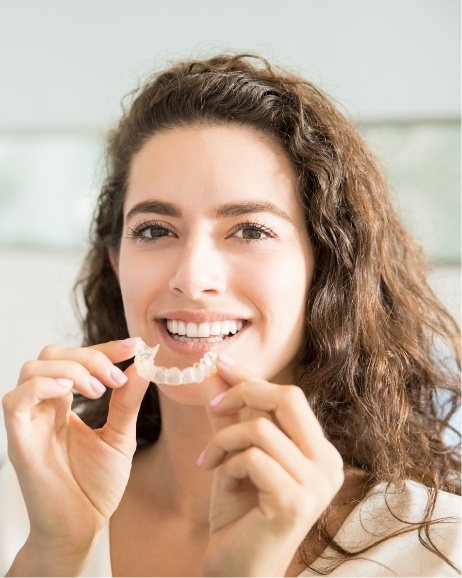 Smiling young woman holding Invisalign tray near her mouth