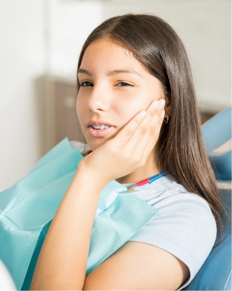 Teenage girl in dental chair holding her cheek in pain