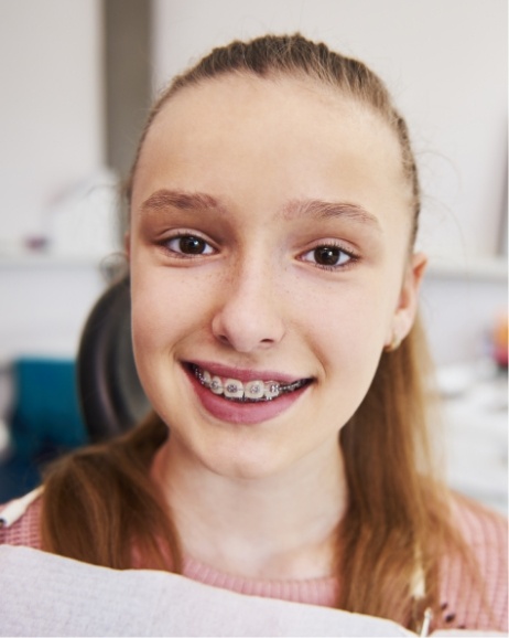 Girl in dental chair smiling with traditional braces